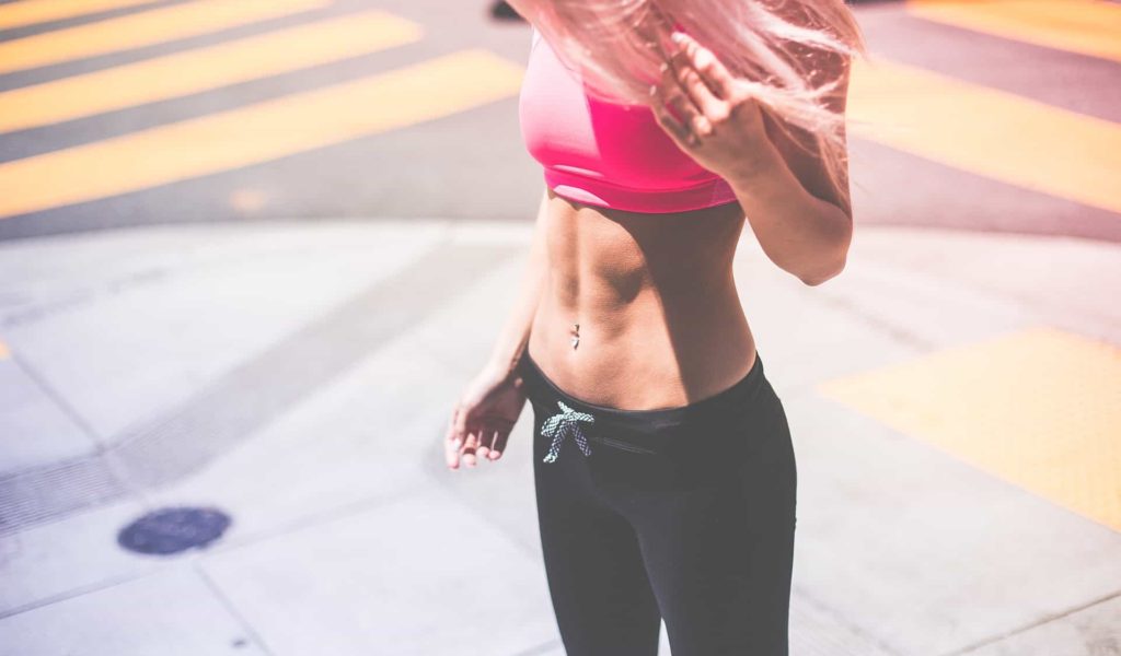 woman in pink sports bra looking down at her abs