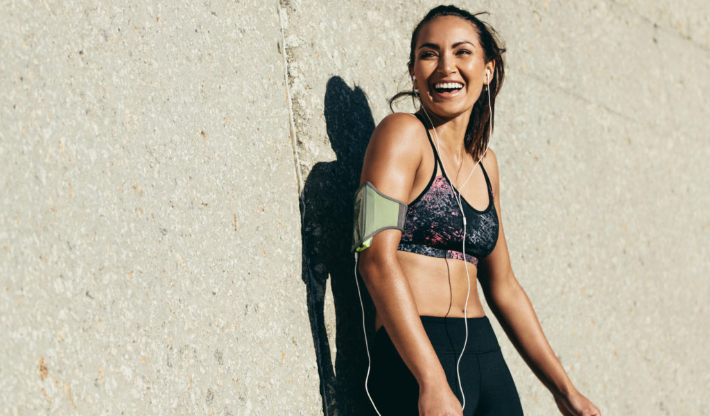 woman laughing after a hard workout leaning against concrete wall