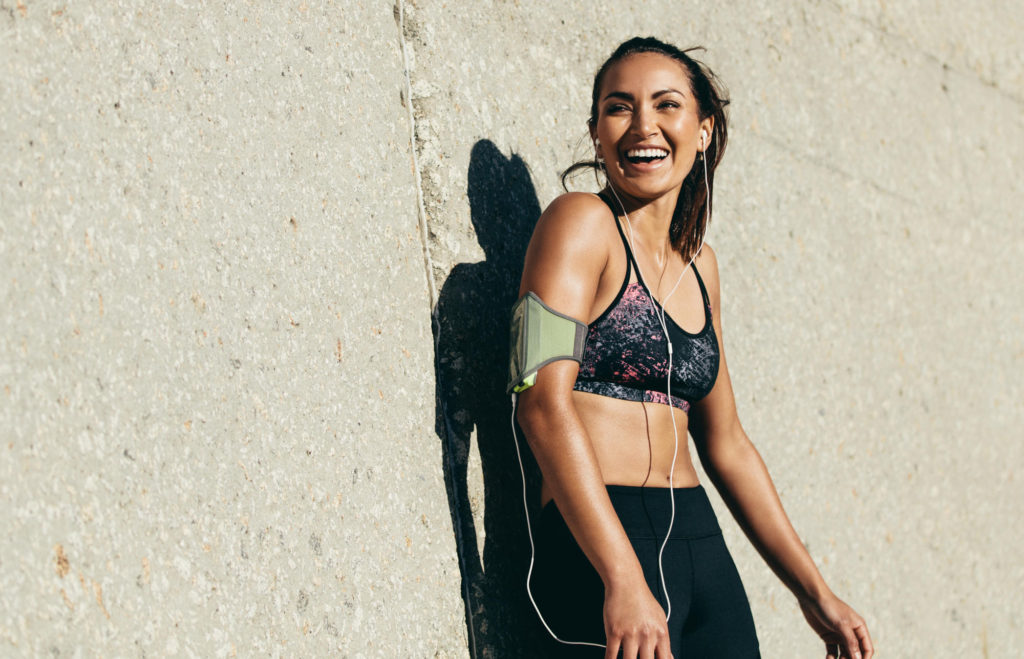 woman laughing after a hard workout leaning against concrete wall