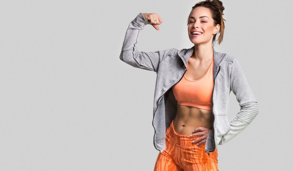 woman smiling and flexing arm in front of gray background