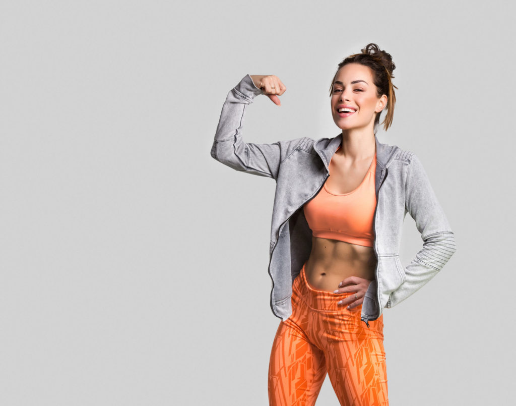 woman smiling and flexing arm in front of gray background
