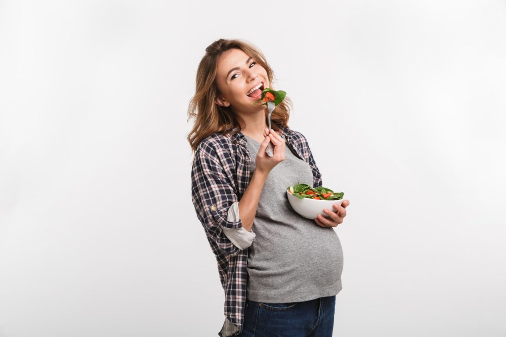 pregnant woman smiling and eating salad