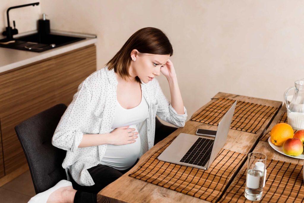 Stressed pregnant woman doing research on her laptop