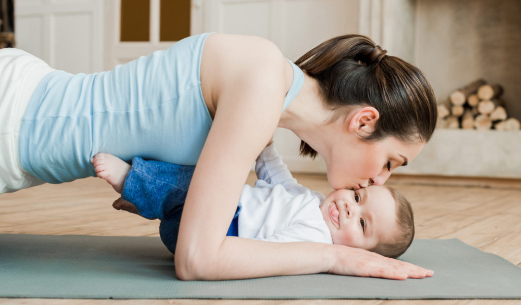 mom kissing baby while working out in plank