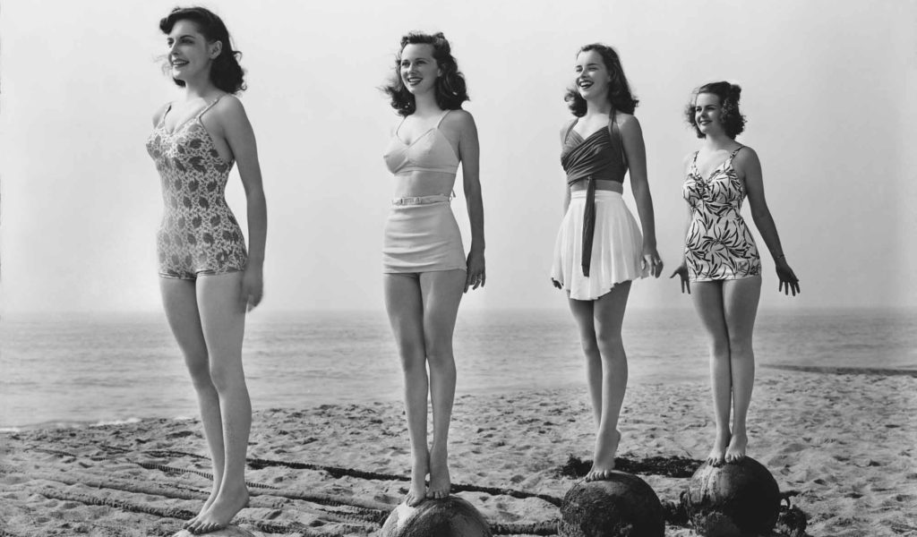 four 1940s women standing on balls on beach