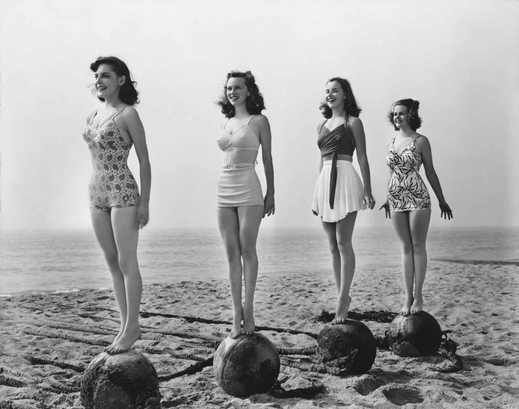 four 1940s women standing on balls on beach