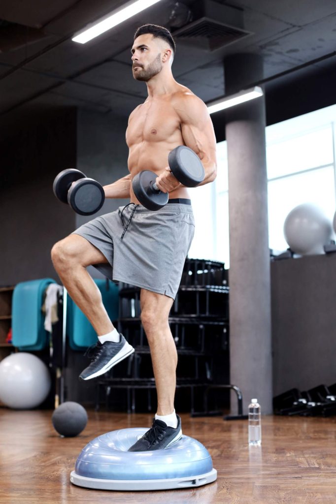 Man doing curls while standing on balance ball