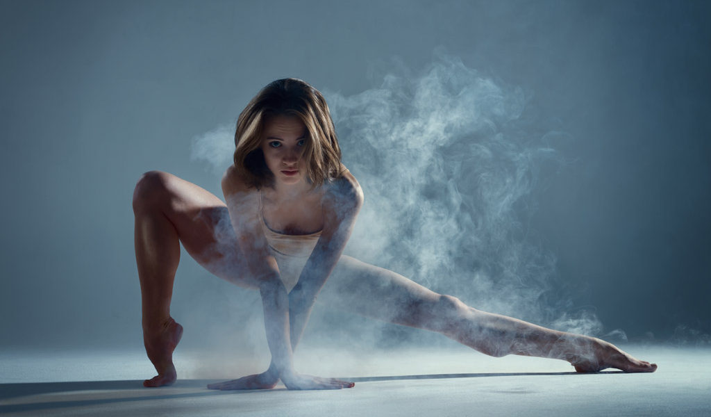 dancer in low side lunge with smoke and a blue background