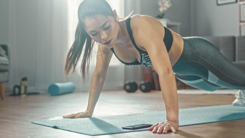 woman doing push ups and checking workout structure on phone in living room
