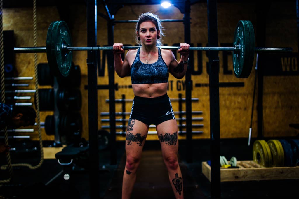 tattooed woman using progressive overload on barbell squats
