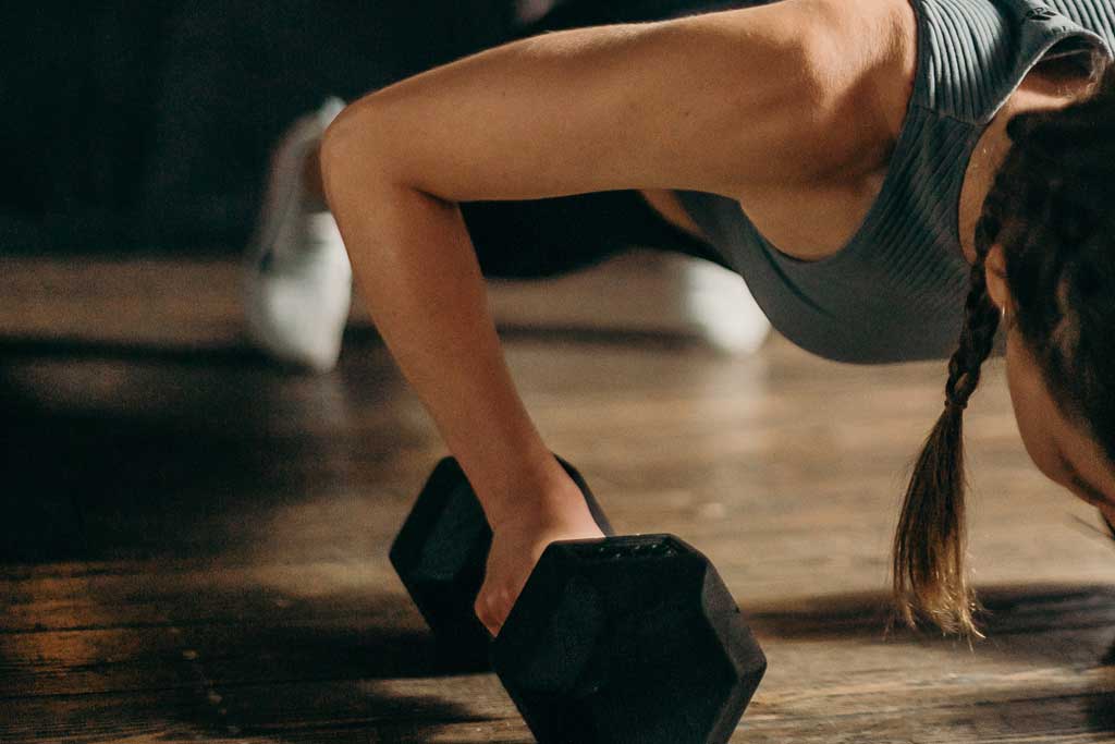 close up of woman with braids doing push ups on dumbbells