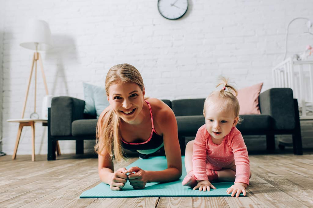 fit mom and bab doing workout planks looking at camera smiling