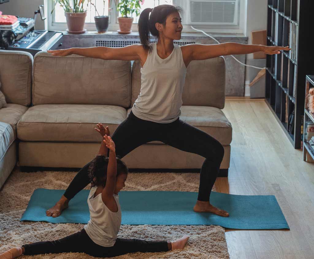 mom doing yoga in living room next to daughter doing split